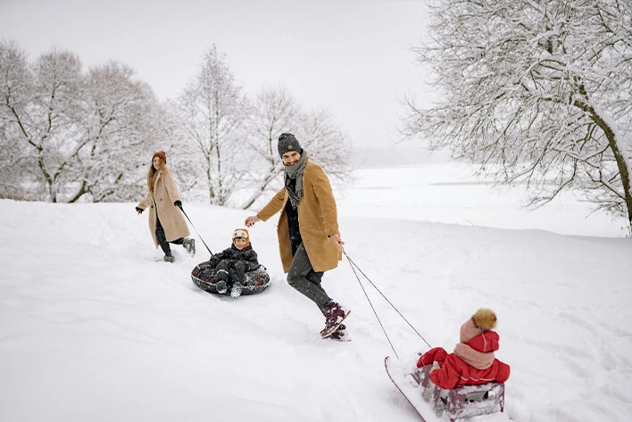 A Man and a Woman Pulling Sled on the Snow with their Children